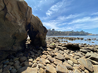 Unstable arch on boulder covered beach with La Jolla Point - Nestor marine terrace in distance.